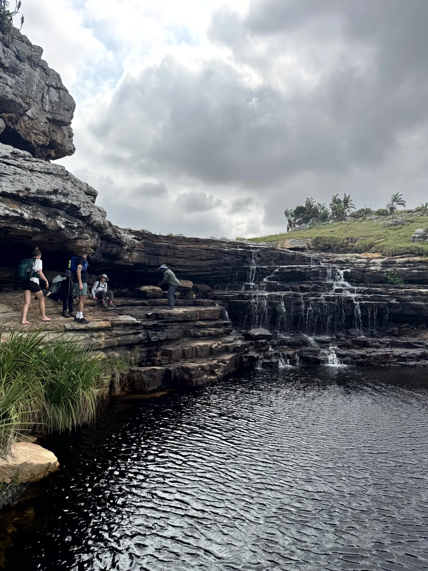 Hikers exploring cascading rock pools with natural waterfall