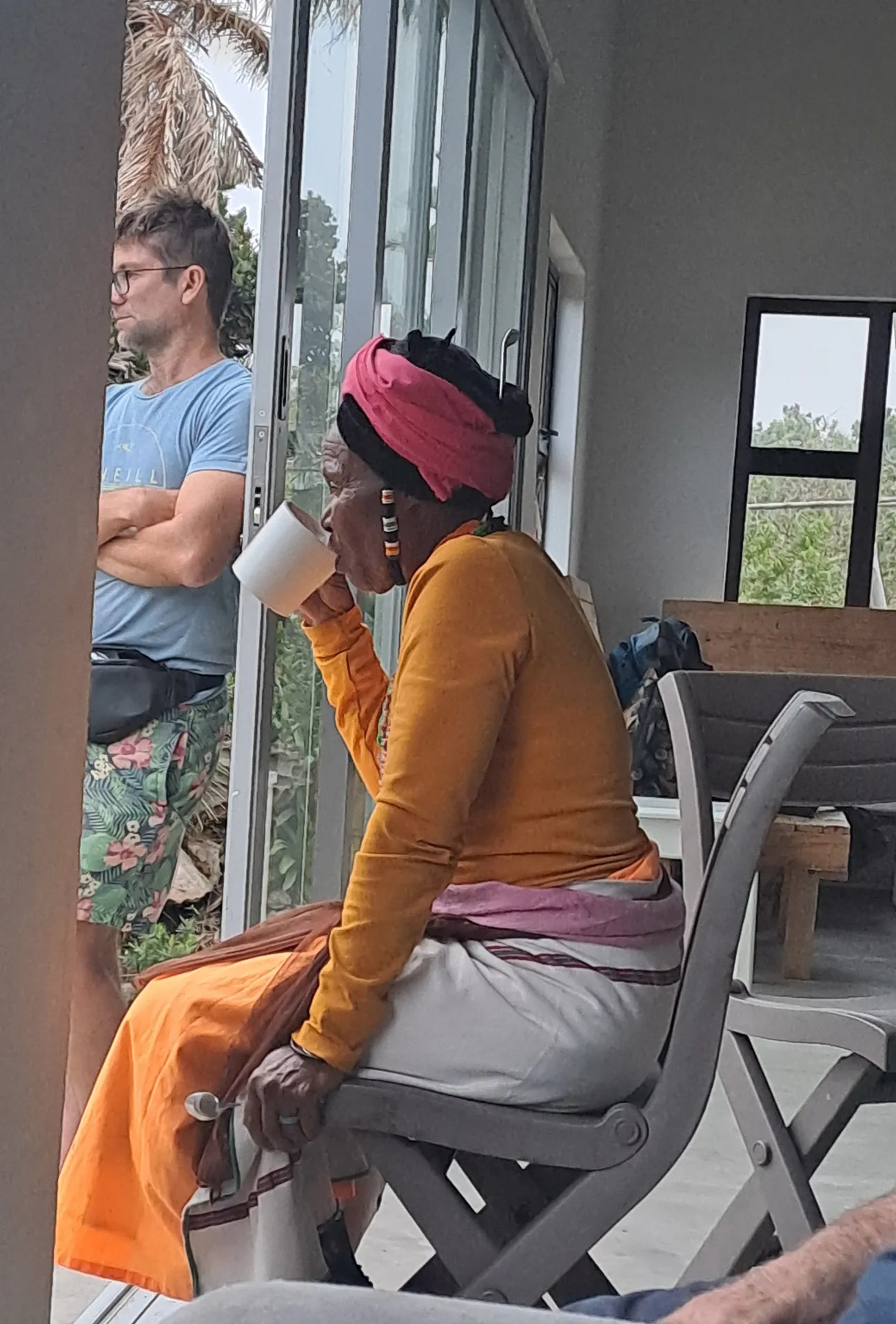 Woman in orange dress with pink headwrap drinking tea on patio